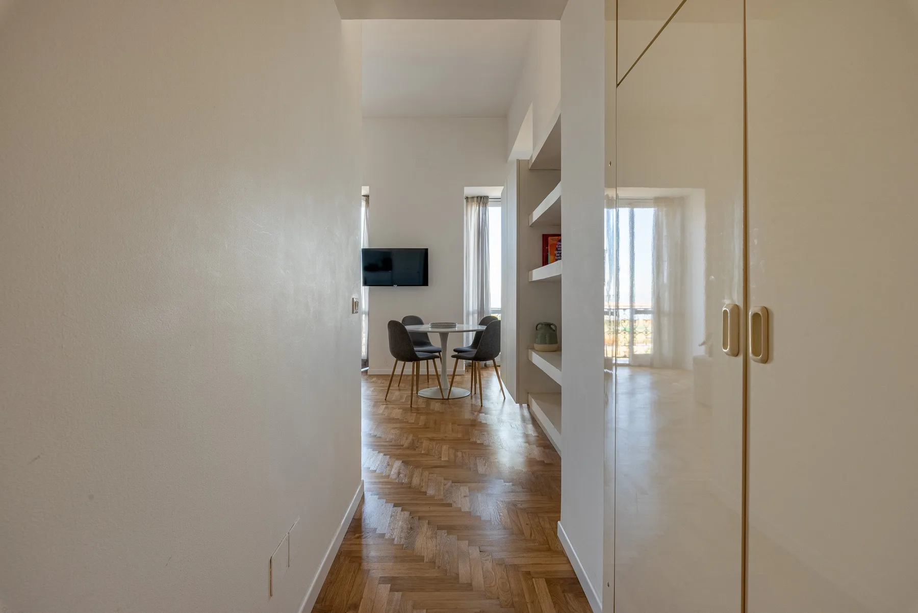 A dining area with a table and chairs sits beyond a bright hallway.