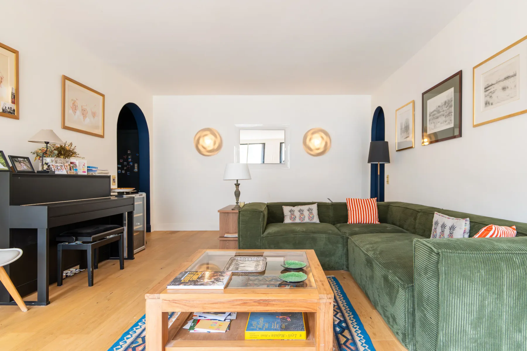 Una sala de estar con asientos verdes, un piano y una mesa baja de madera.