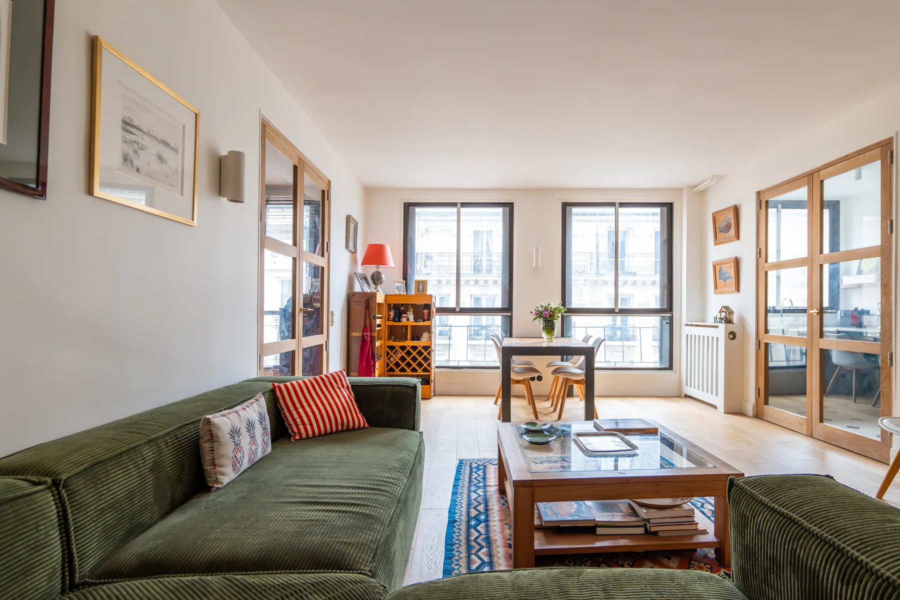 Una sala luminosa con asientos verdes, una mesa de centro y grandes ventanas.