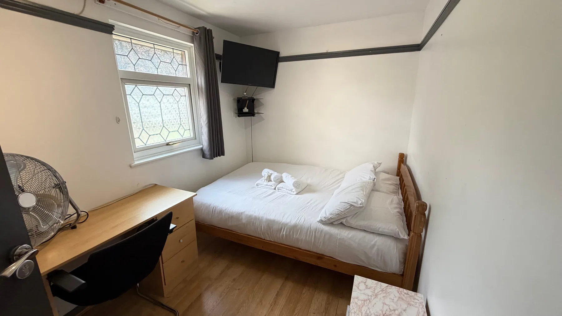 A bedroom with a bed, desk, and window.