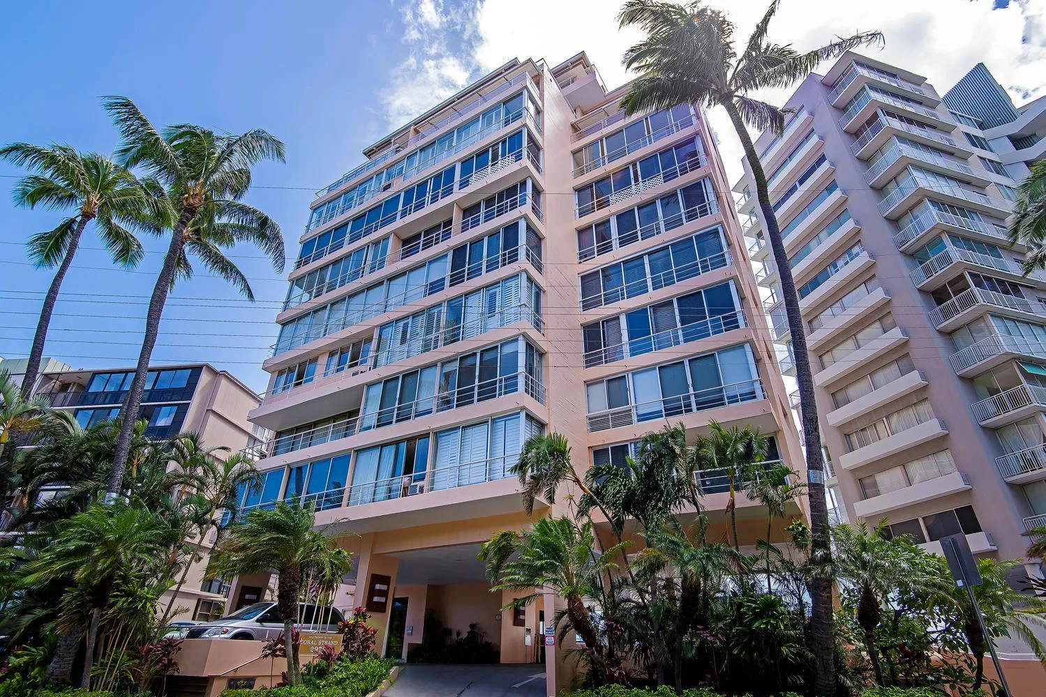 Un edificio de varios pisos con balcones se alza entre palmeras.