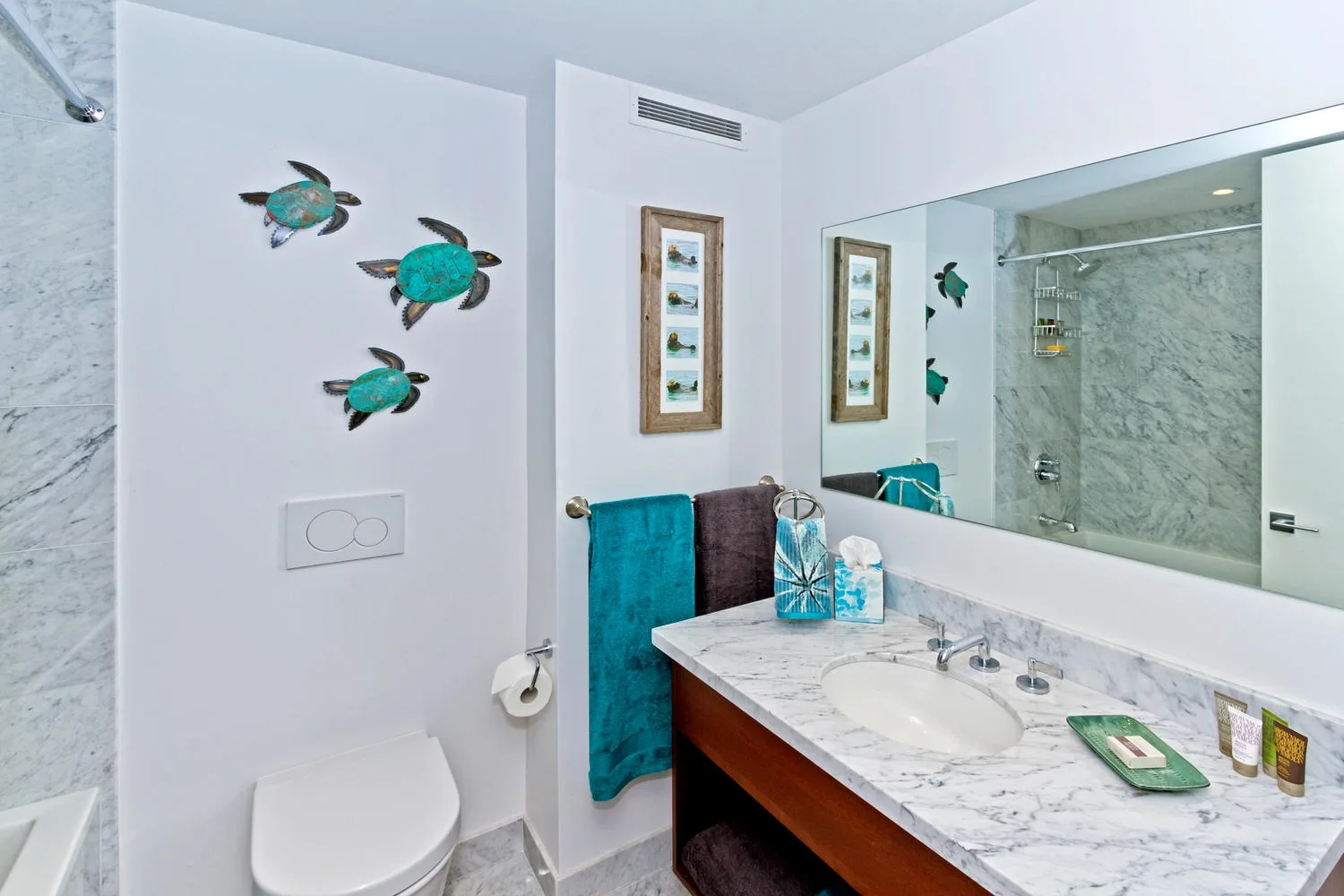 Un baño luminoso con tocador de mármol, espejo de pared y toallas turquesas.