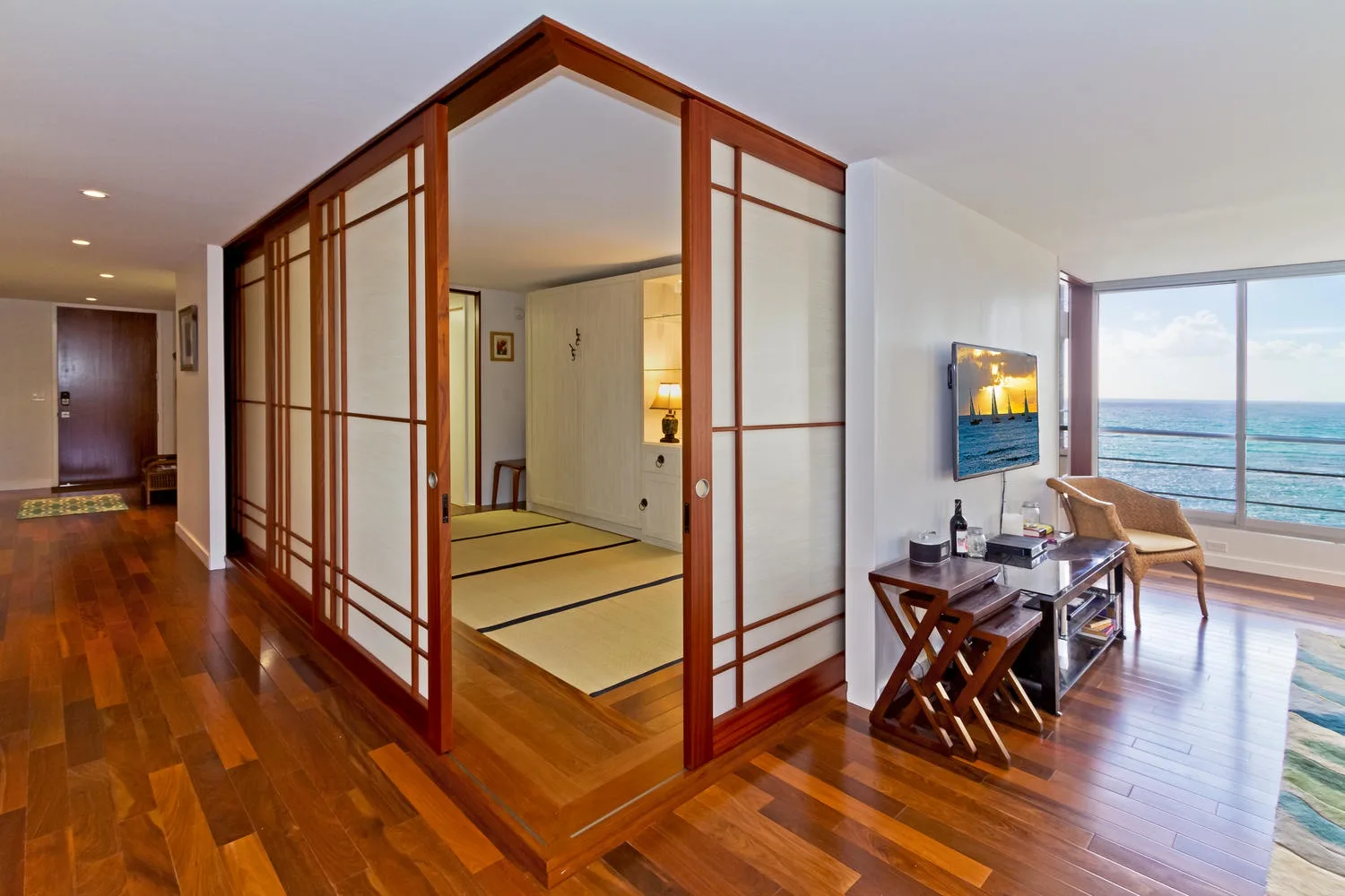 Una luminosa sala tiene suelo de madera, paneles plegables y vistas al mar.