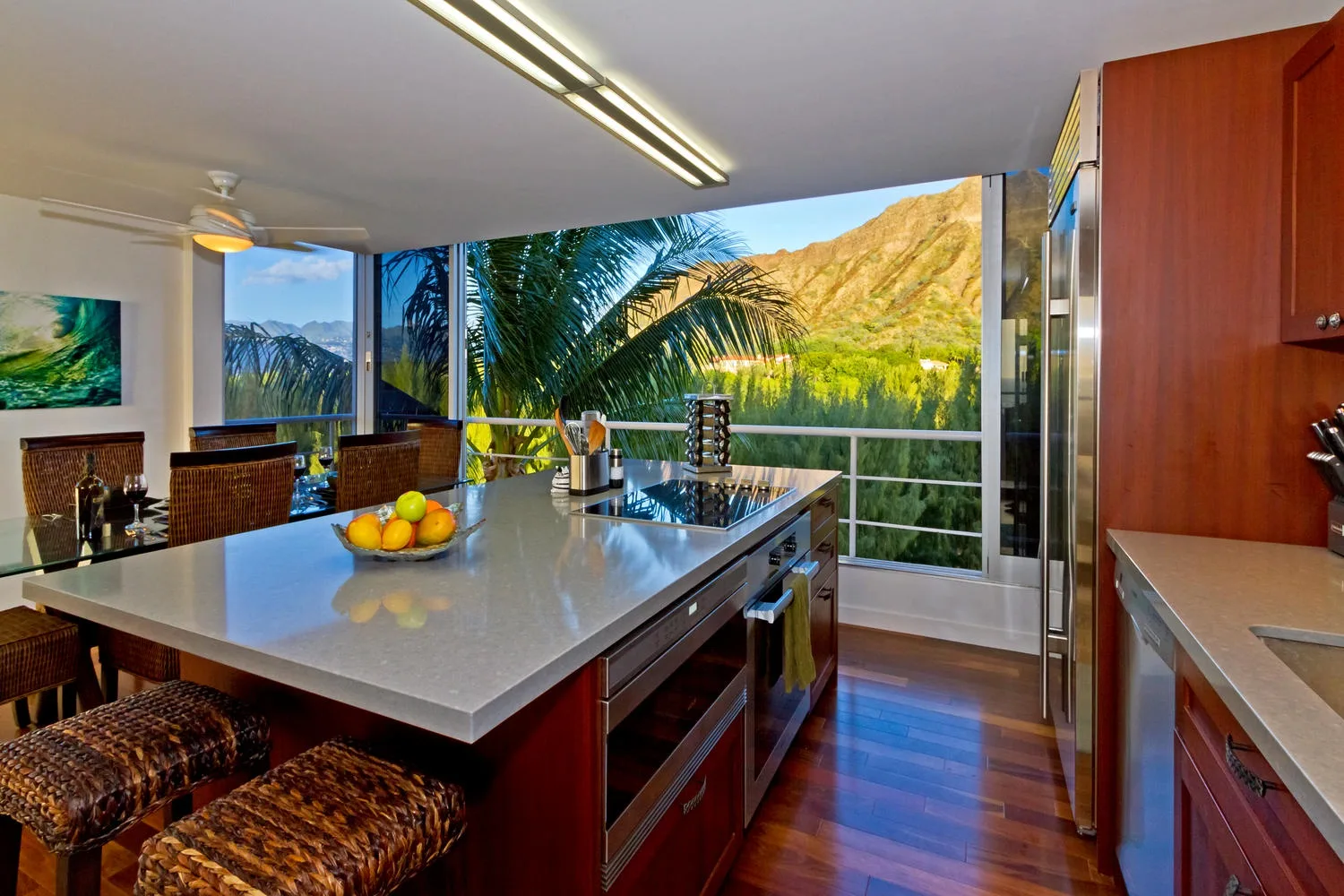 A kitchen with a central island and large windows overlooking a green mountain landscape.