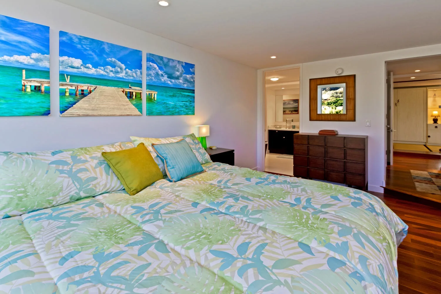Un dormitorio con una cama estampada, almohadas de colores y arte de playa tropical.