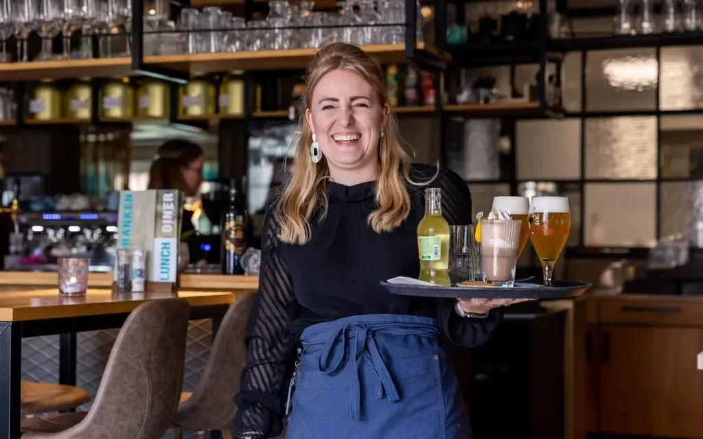 A woman carries a tray of drinks in the restaurant.