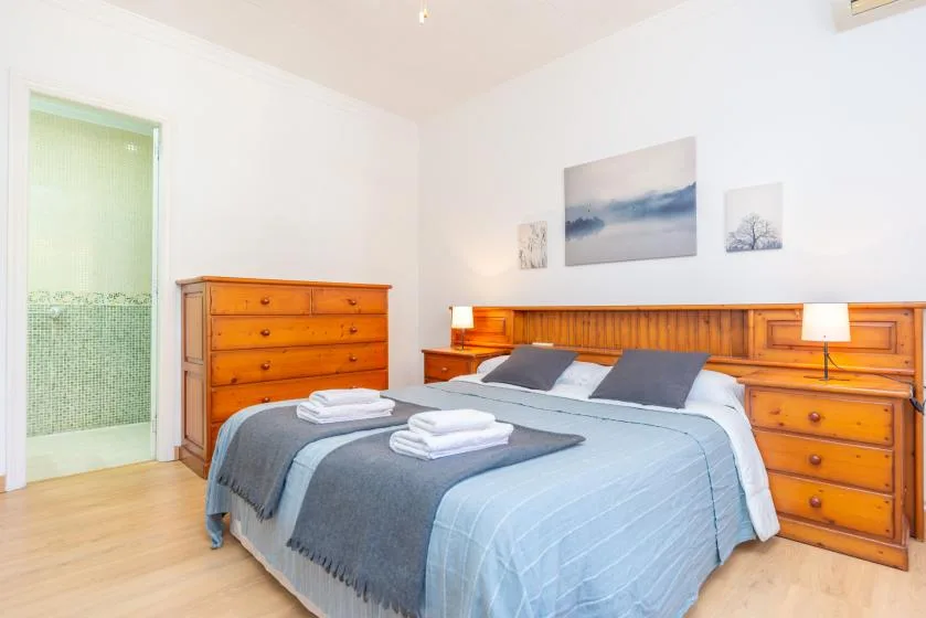 A bright bedroom with a neatly made bed and wooden dressers.