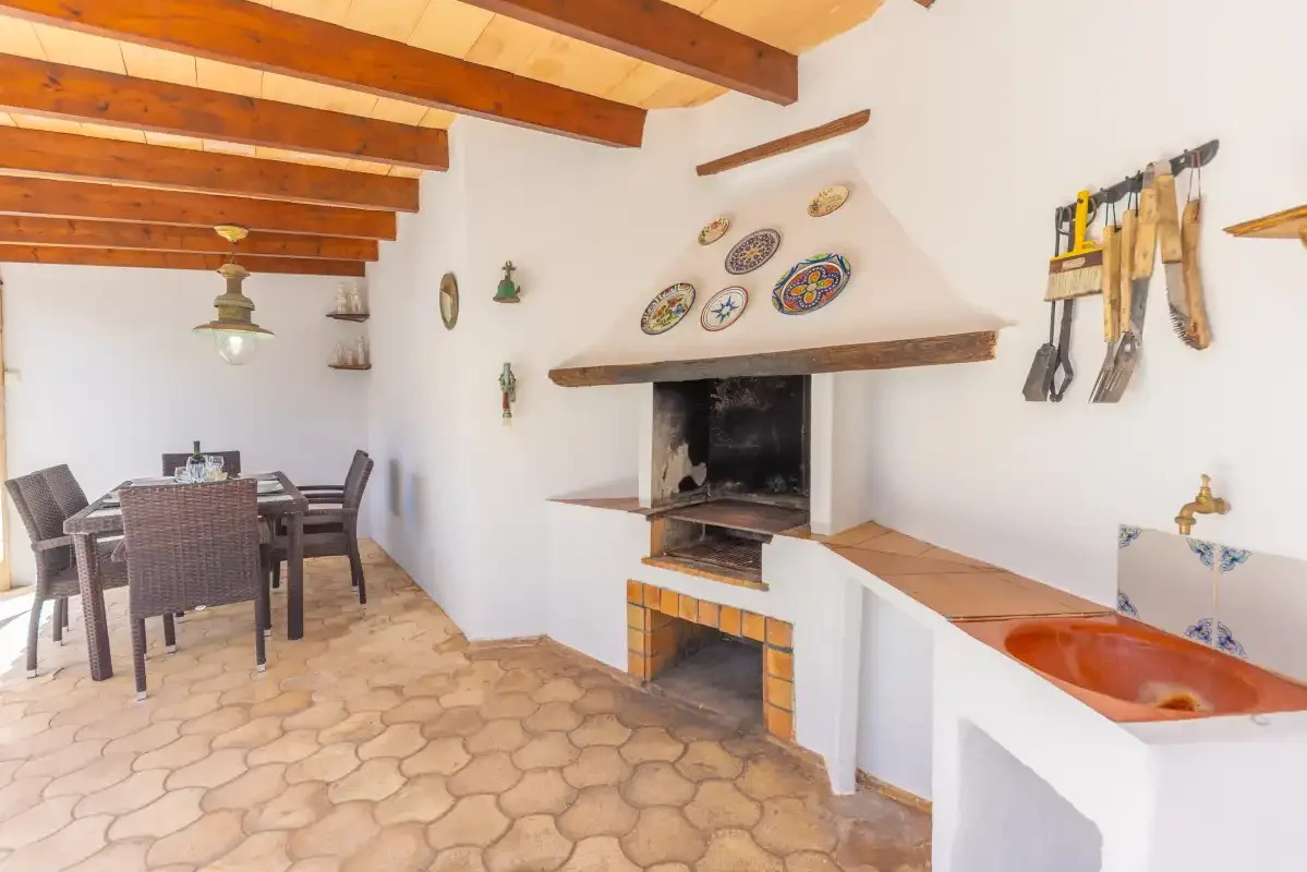 A rustic dining and kitchen area features a table, fireplace, and terracotta sink.