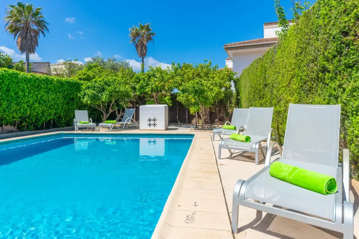 An outdoor swimming pool is bordered by lounge seating and tall green hedges.