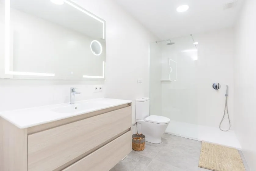 A bright bathroom with a wide vanity, toilet, and glass shower area.