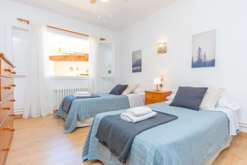 A bright bedroom with two beds and a small bedside table.