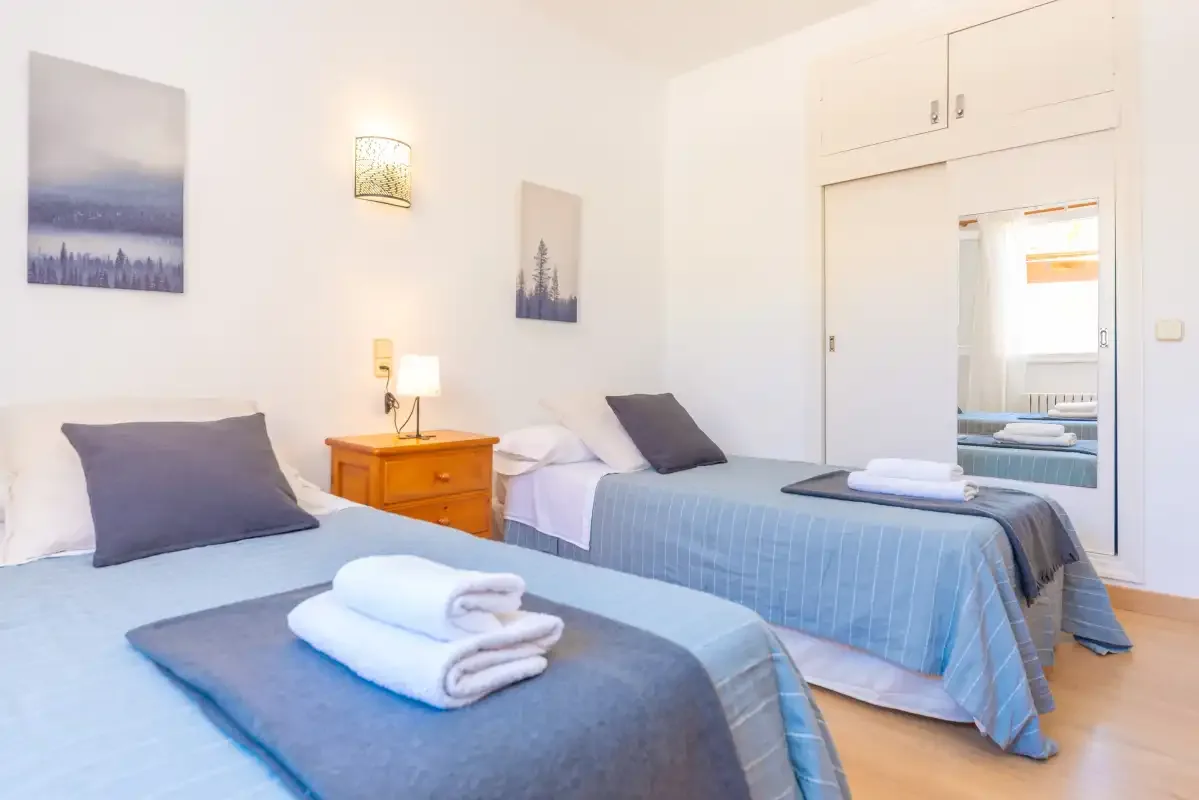 A bright bedroom with two beds and folded towels.