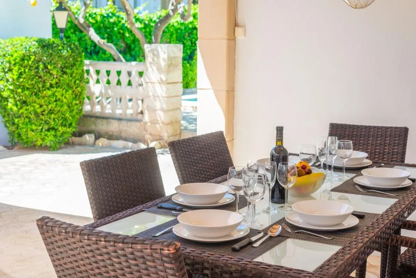 A set dining table sits beside a bright patio with green hedges.