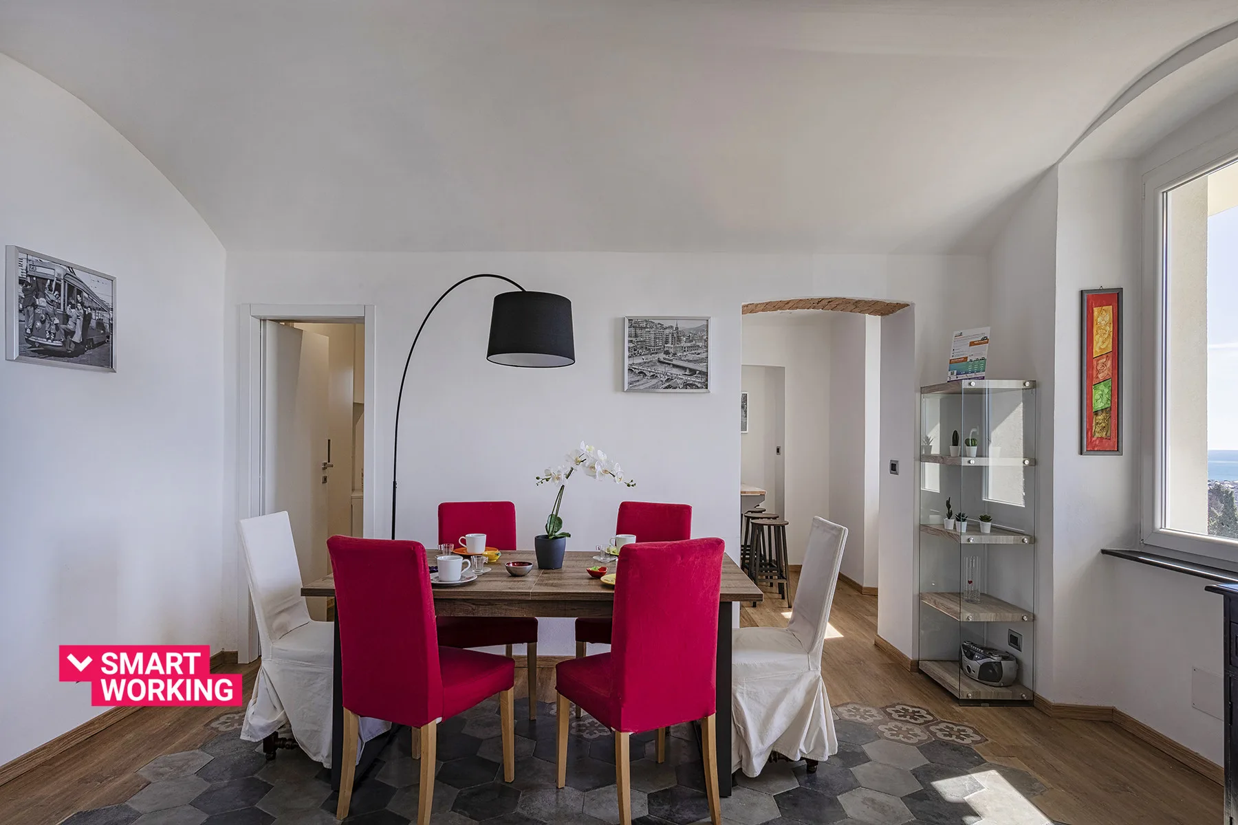 Comedor con una mesa, asientos rojos y una gran lámpara de pie arqueada.