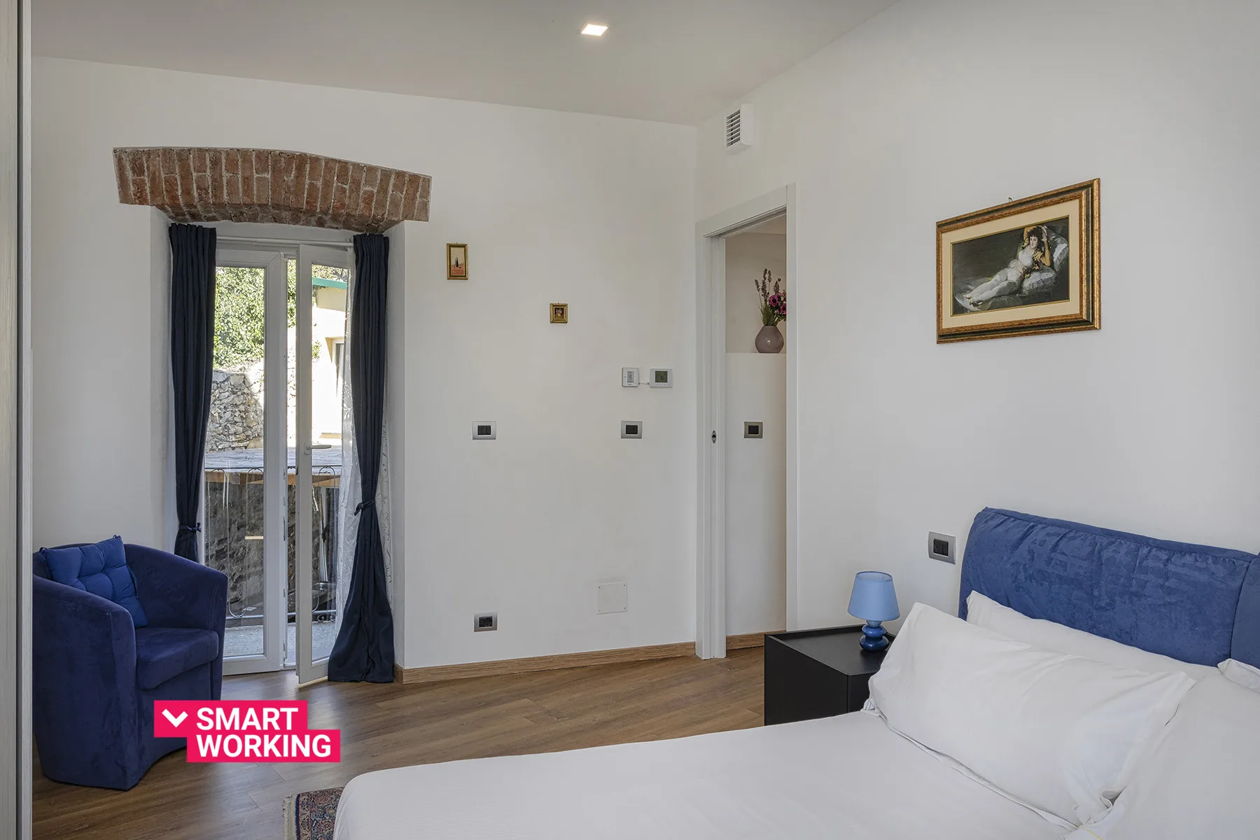 Un dormitorio con una cama, asientos azules y puertas de vidrio que dan a un balcón.