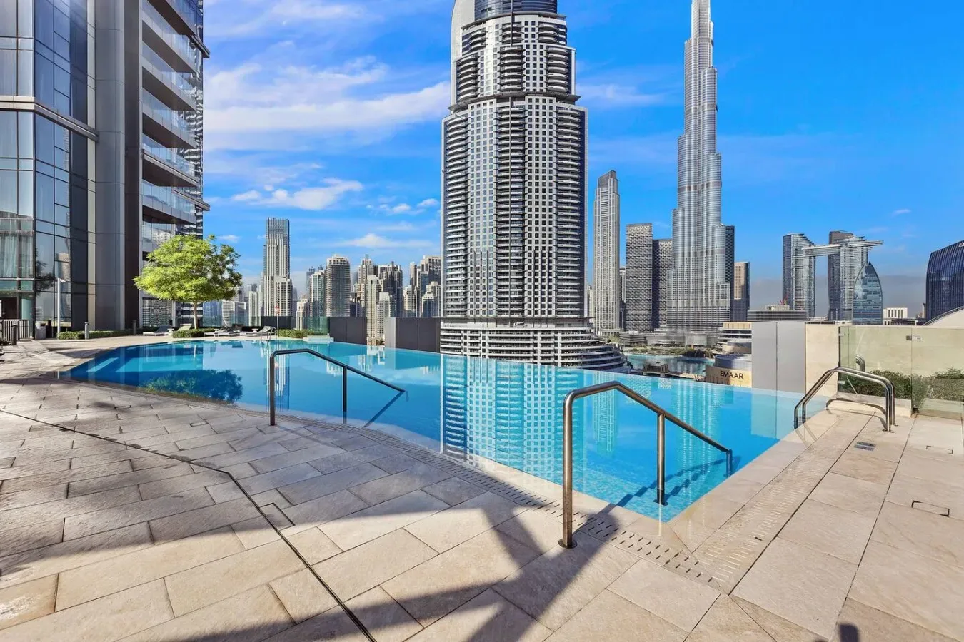 A rooftop swimming pool overlooks a city skyline under a clear blue sky.