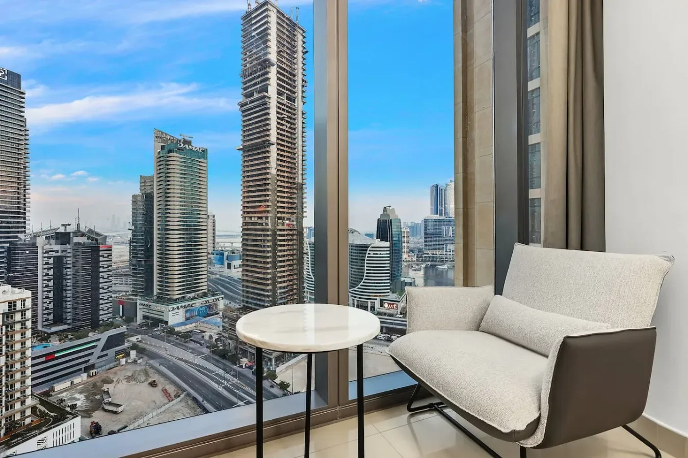 A bright sitting area beside floor-to-ceiling windows overlooks a city skyline.