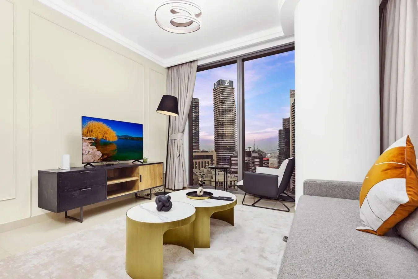 A bright living room with a television, coffee tables, and floor-to-ceiling windows.