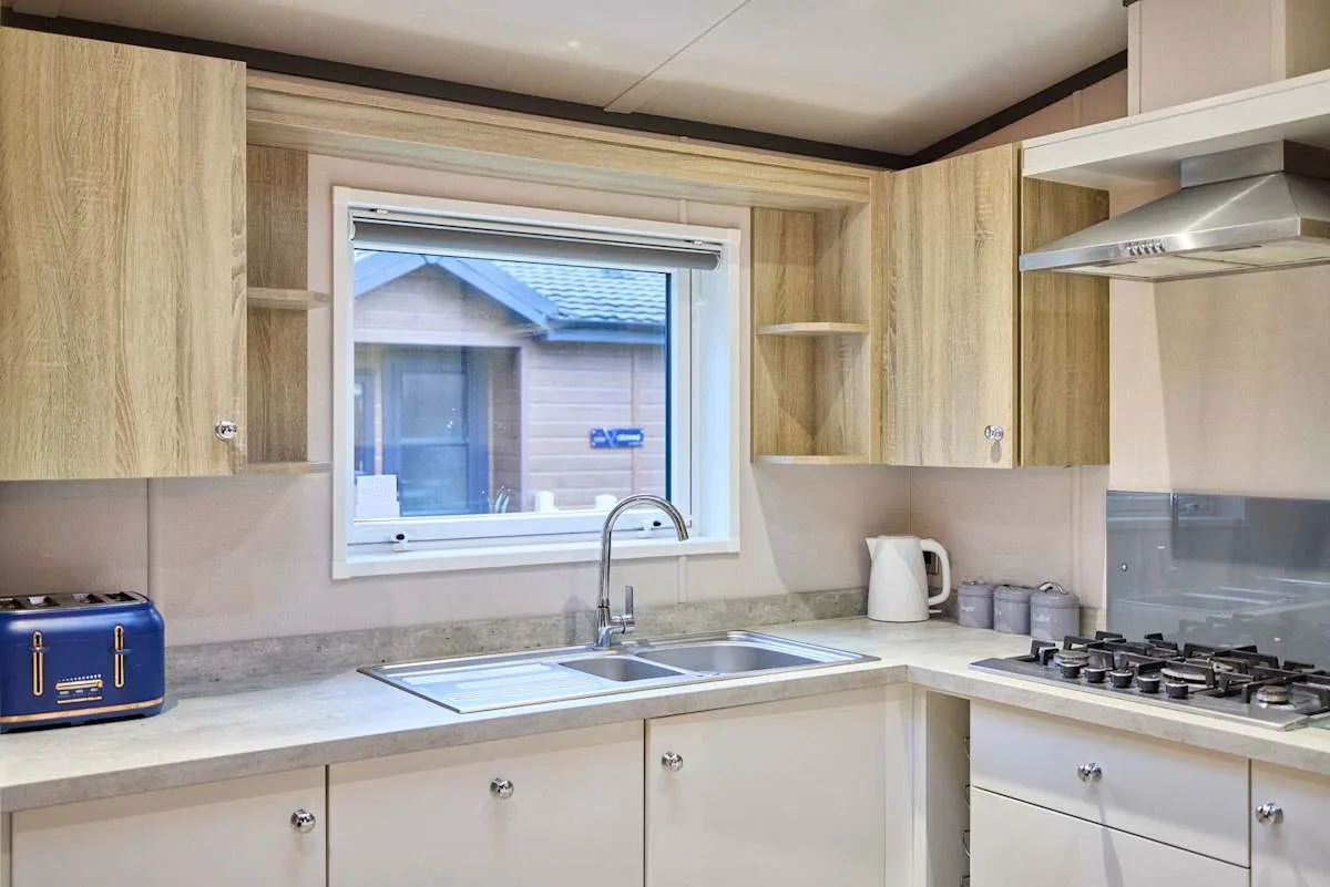 Una cocina con gabinetes de madera clara, un fregadero y una estufa de gas.