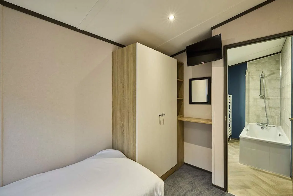Dormitorio con cama, armario y un baño contiguo visible a través de la puerta.