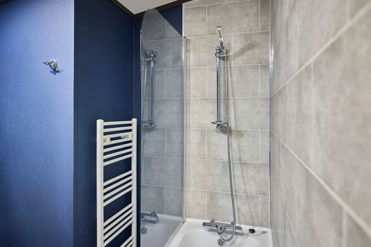 Un baño alicatado con ducha y un radiador toallero blanco.