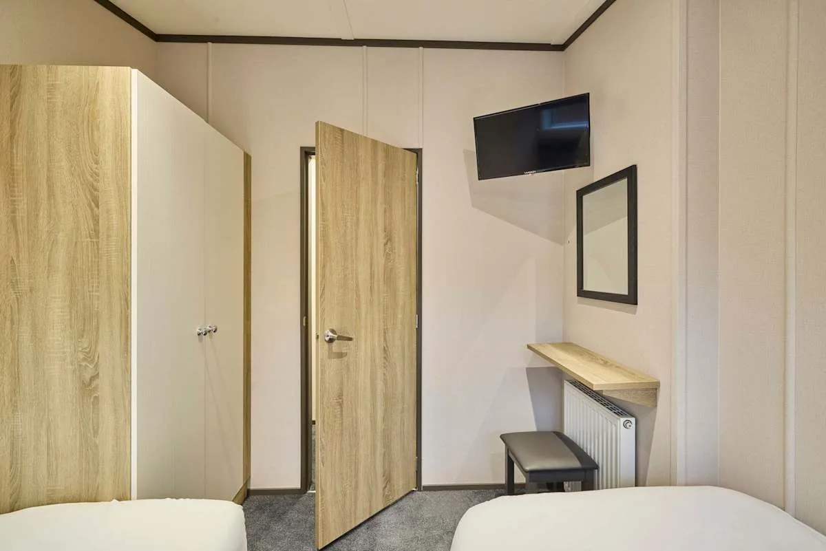 Un dormitorio compacto con dos camas, un televisor en la pared y un pequeño escritorio.