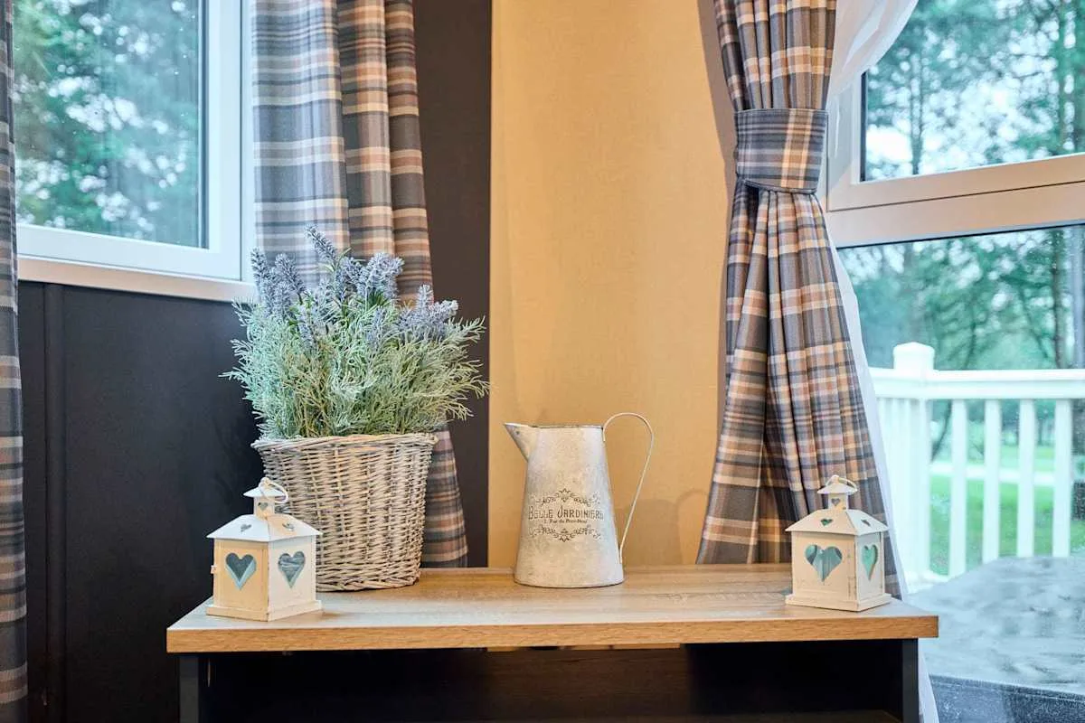 Una mesa junto a la ventana muestra una planta en maceta y faroles decorativos.