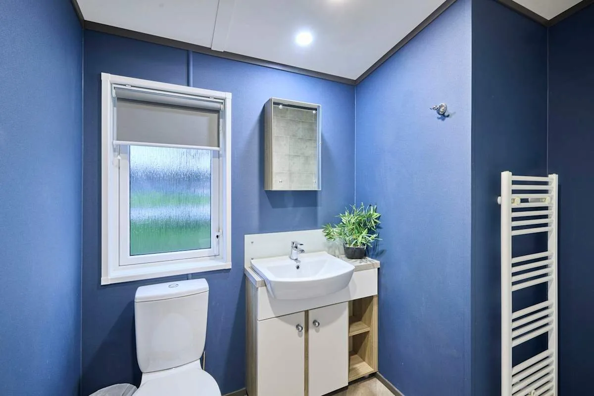 Un baño azul con lavabo, inodoro y toallero de pared.