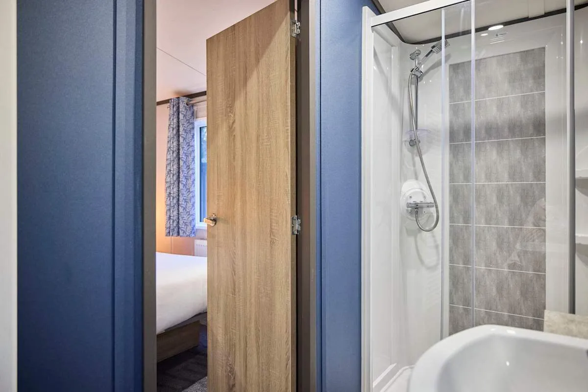 Un baño con ducha de vidrio y una puerta de madera abierta.