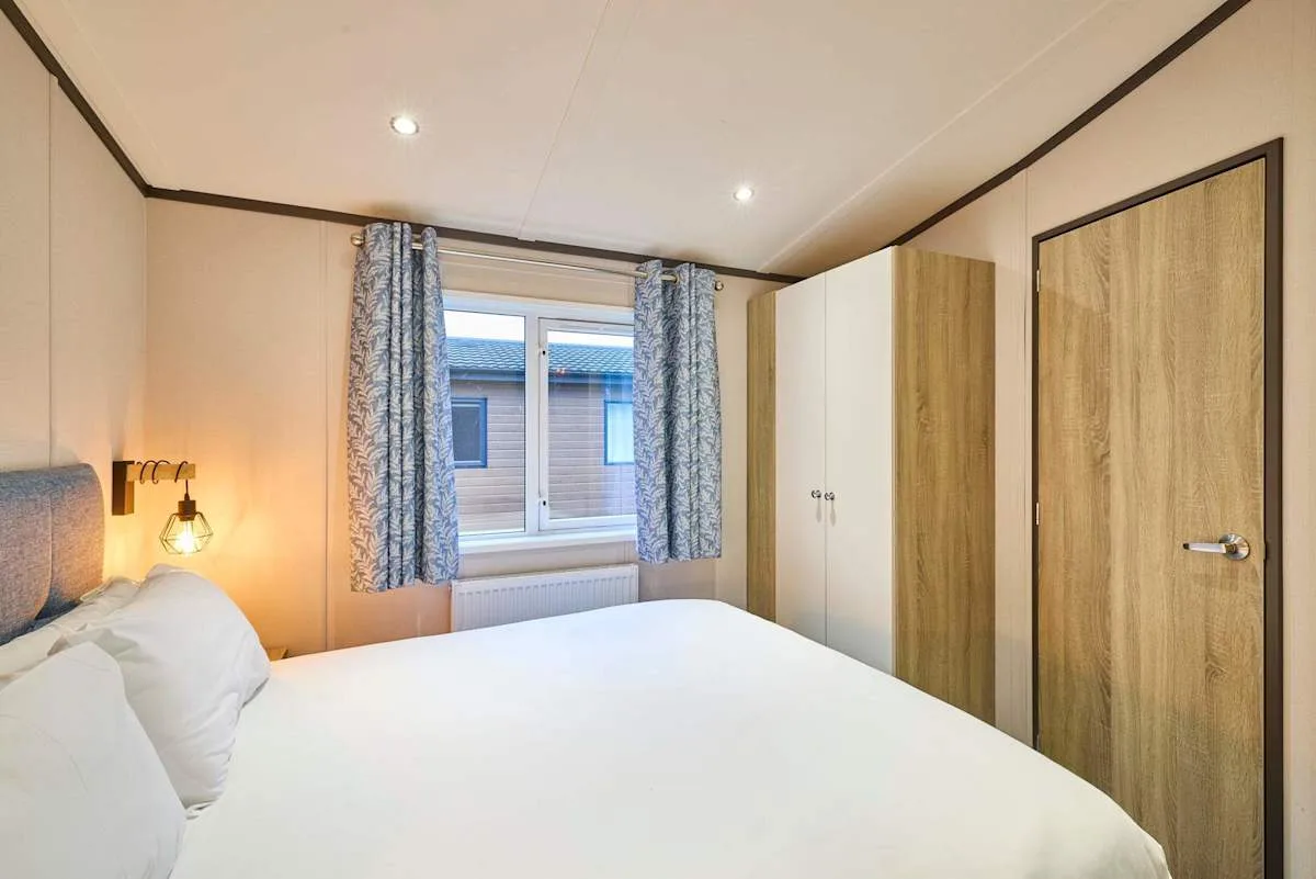 Dormitorio con una cama blanca, una ventana con cortinas y un armario.