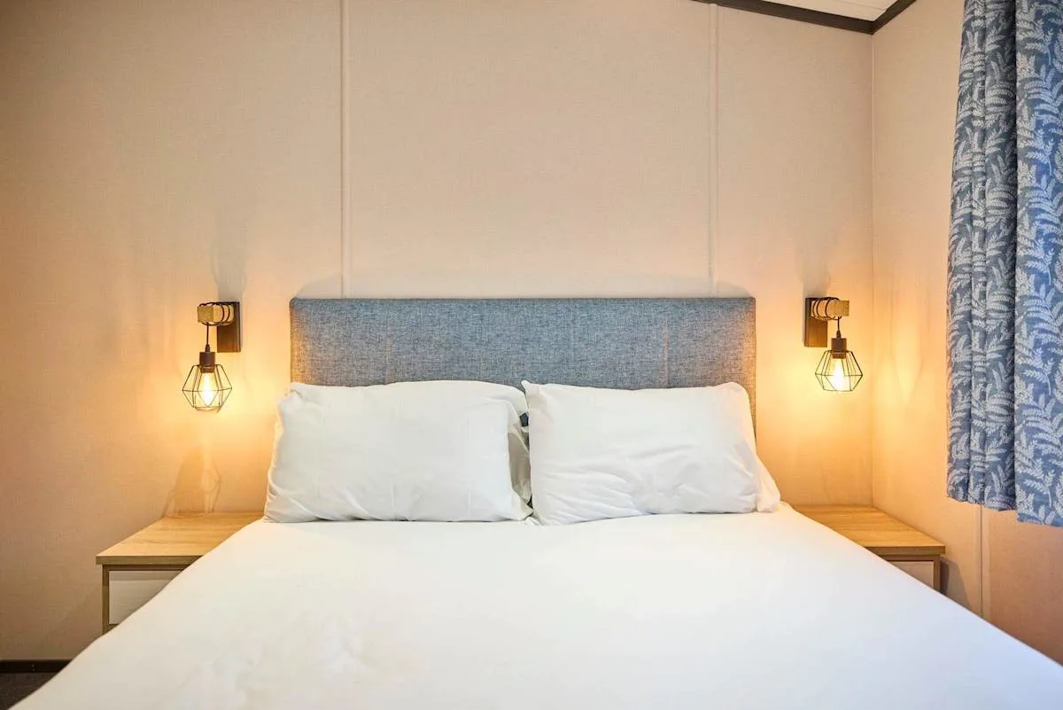 Un dormitorio con una cama bien tendida y luces de pared a ambos lados.