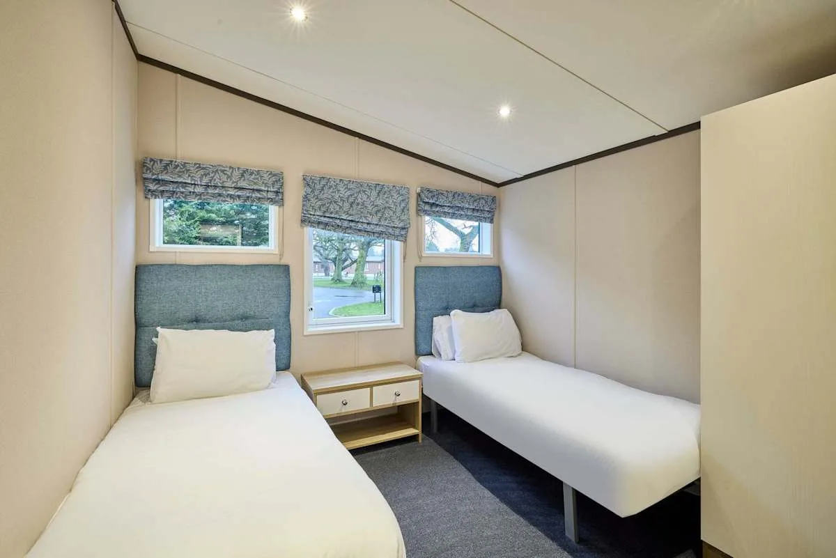 Un dormitorio con dos camas individuales y ventanas con vistas a zonas verdes.