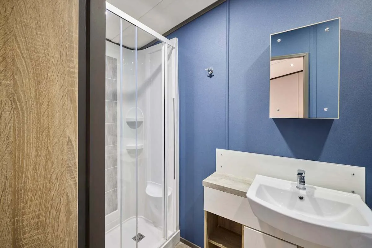 Un baño con una ducha de vidrio y un lavabo blanco junto a paredes azules.