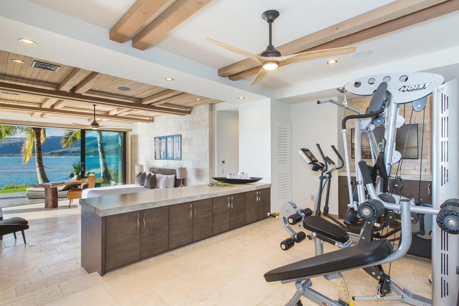 An open living area with a kitchen island and exercise equipment beside a large window.