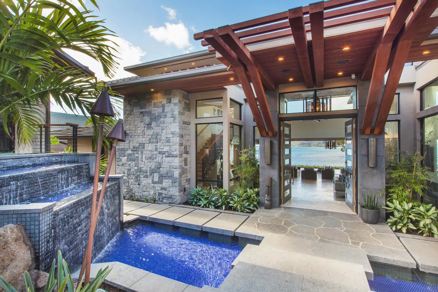 An outdoor pool sits beside a stone patio beneath a wooden pergola.