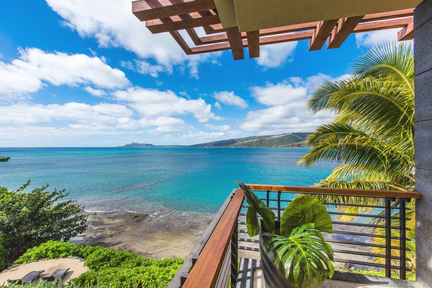 A balcony overlooks turquoise water, with palm leaves beside the railing.