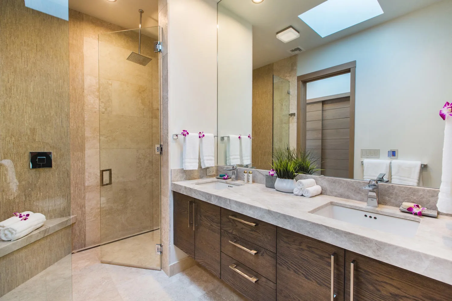 A bright bathroom with a long vanity, sinks, and a glass shower.