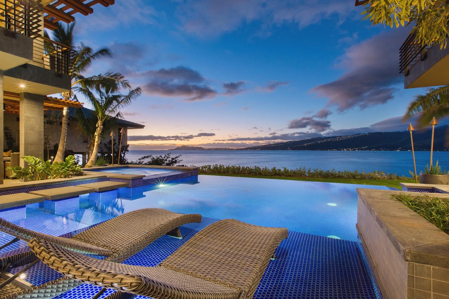 An infinity pool overlooks the water, with lounge seating in the foreground.