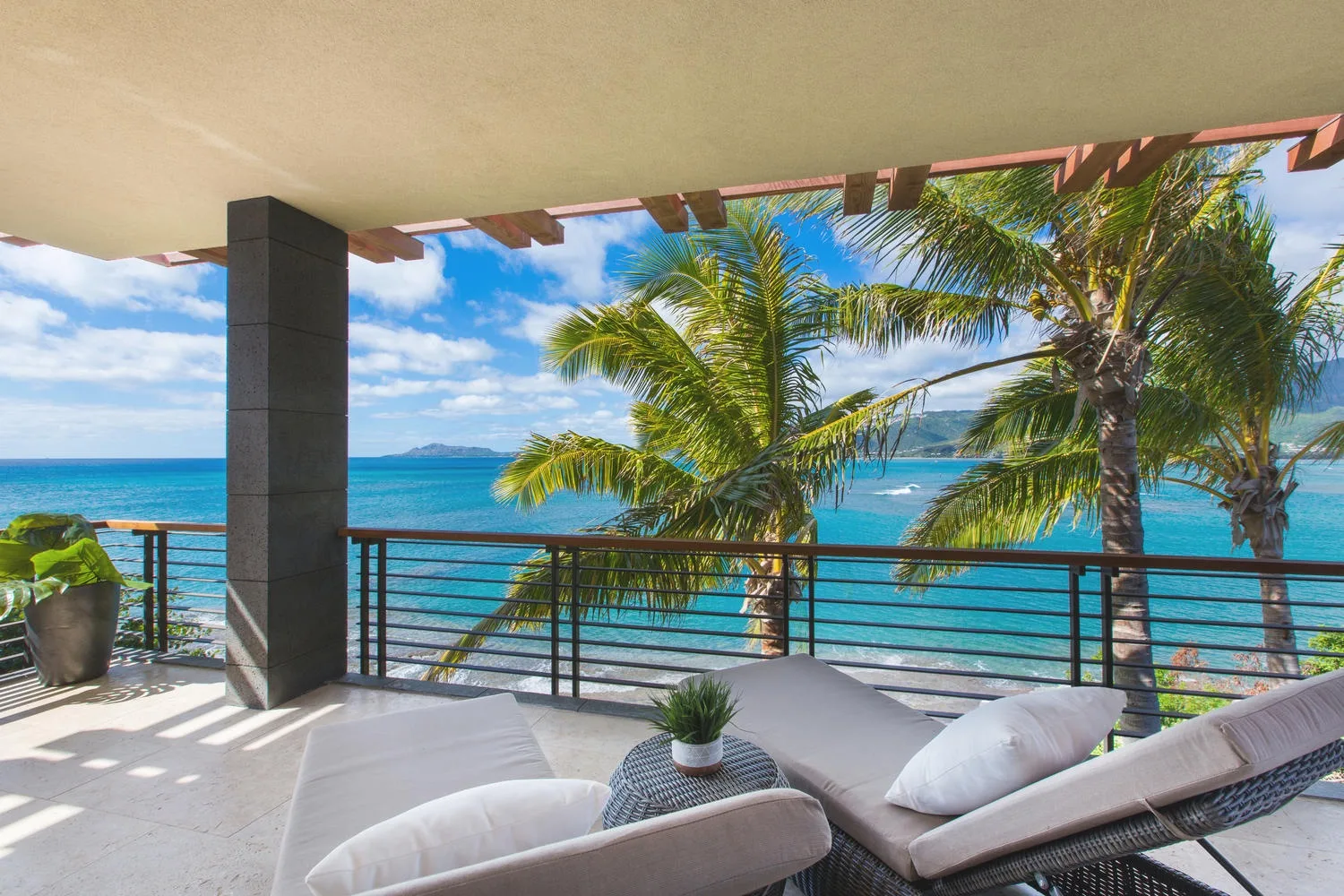 A covered outdoor seating area overlooks palm trees and the ocean.