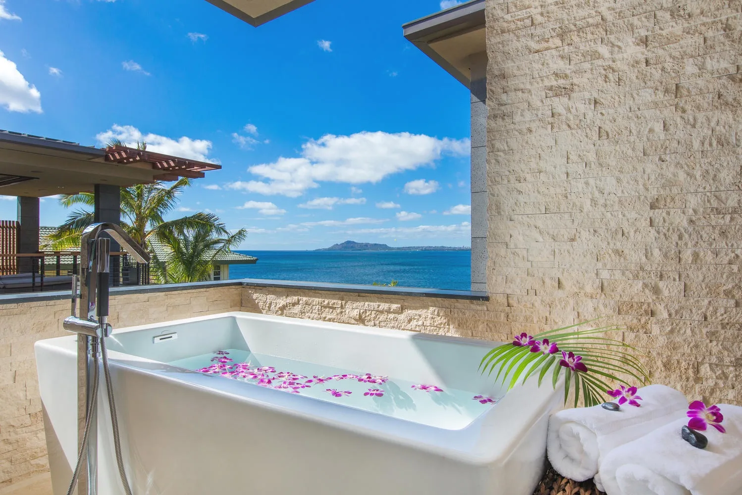 An outdoor soaking tub overlooks the ocean, with flower petals floating in the water.