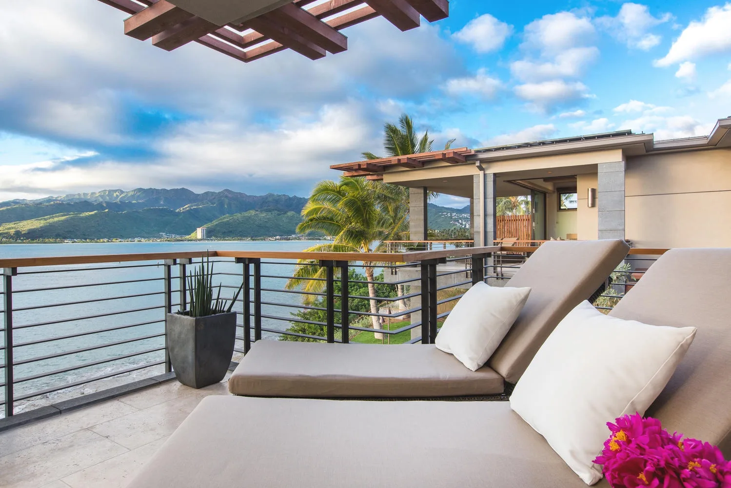 A terrace overlooks the water and distant mountains, with cushioned seating beside the railing.