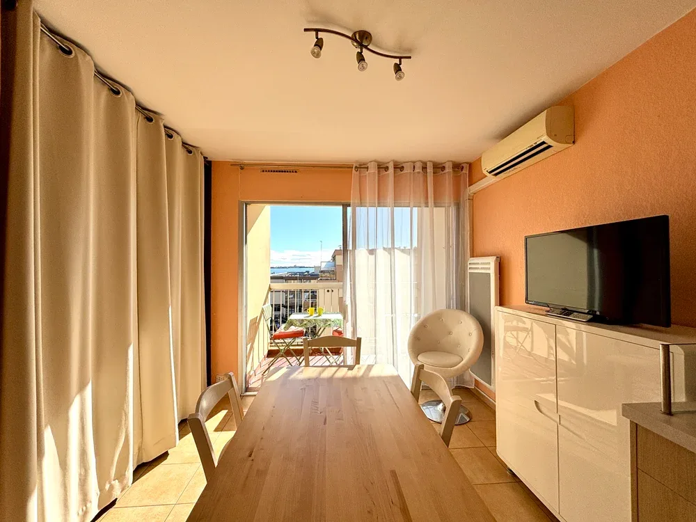 Un comedor luminoso tiene una mesa de madera, asientos y un televisor.
