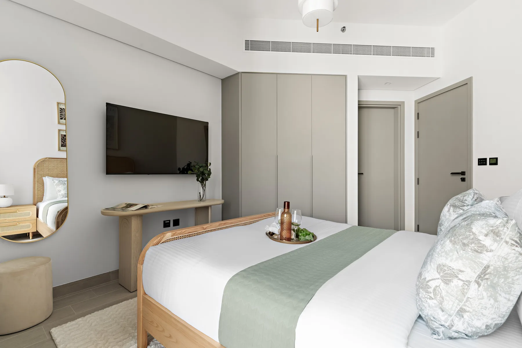 A bright bedroom with a neatly made bed and a wall-mounted television.
