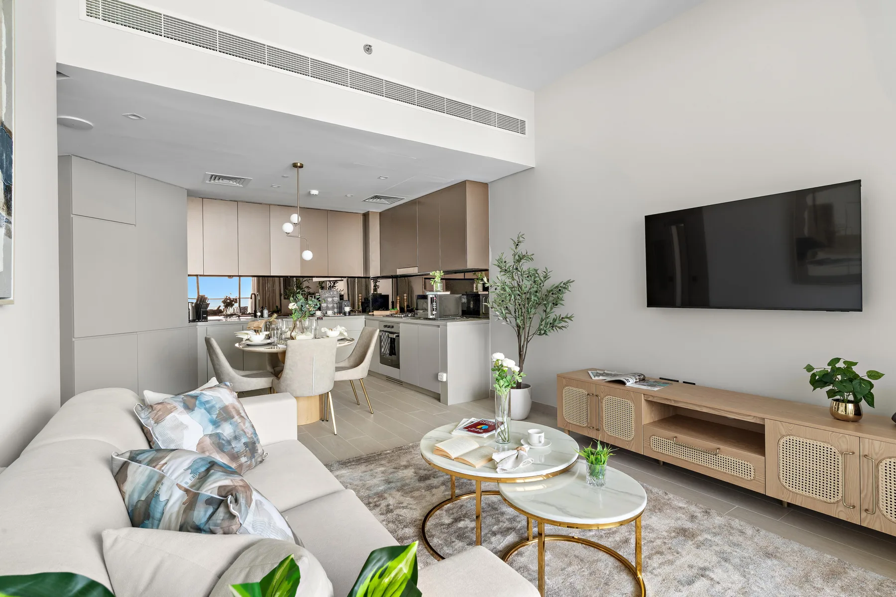 A bright open-plan living room with seating, coffee tables, and a kitchen in the background.