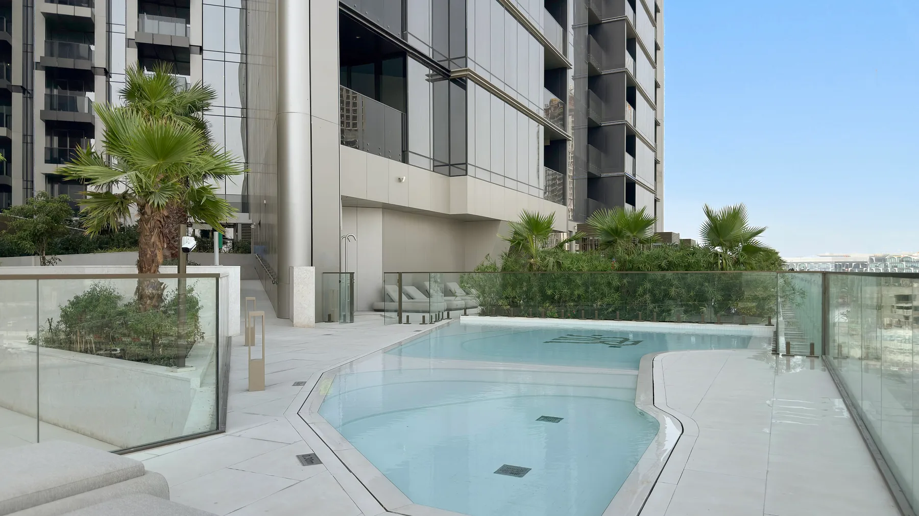 An outdoor swimming pool sits beside a modern building and glass railings.