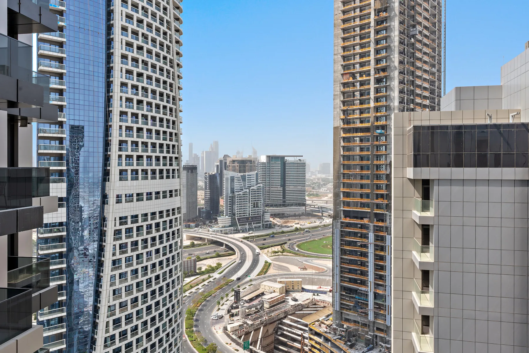 Cityscape view between high-rise buildings, with winding roads and modern towers.