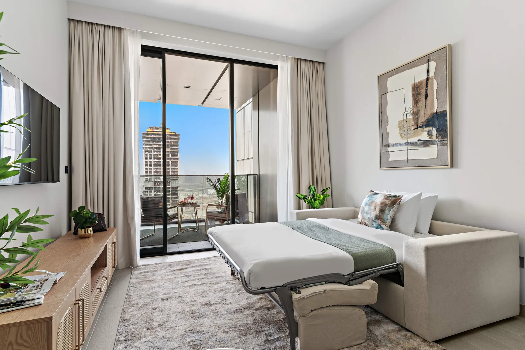 A bright living room with a sofa bed beside sliding glass doors opening onto a balcony.
