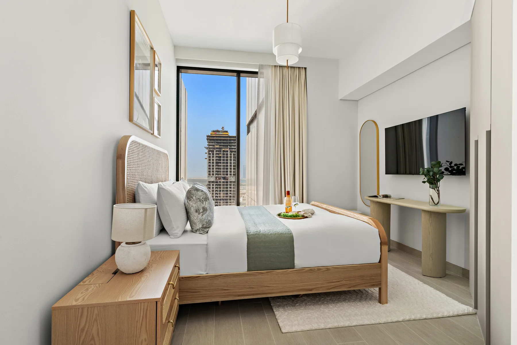 A bright bedroom with a bed, a window, and a wall-mounted television.