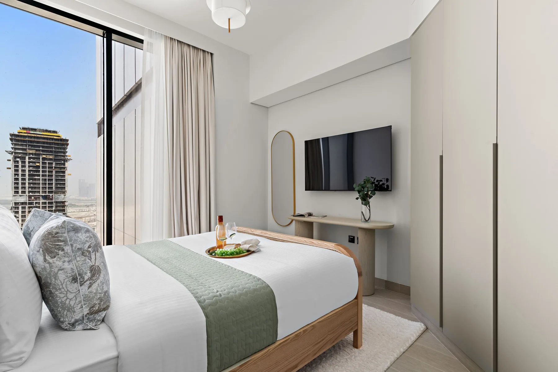 A bright bedroom with a bed, television, and large curtained window.