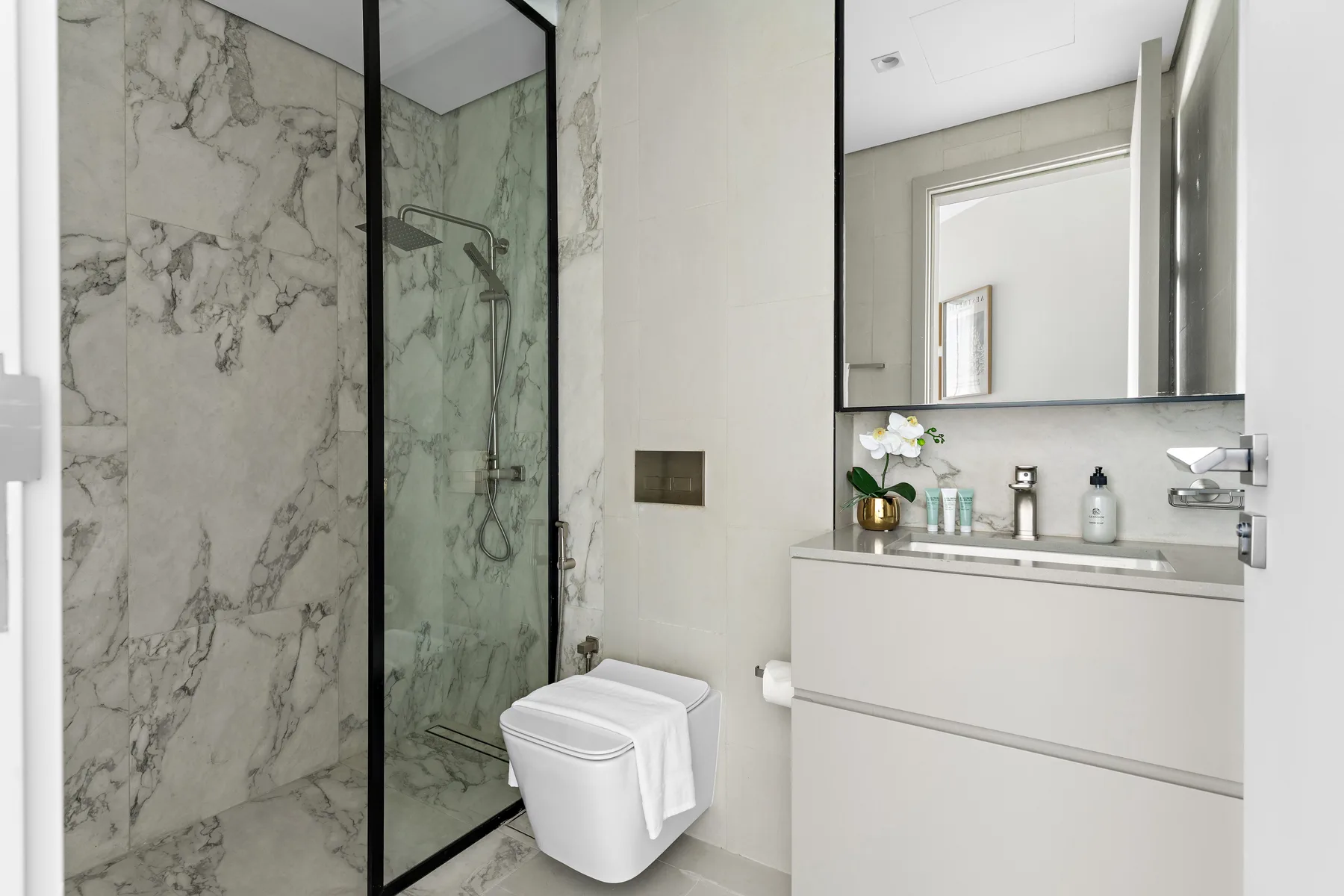 A modern bathroom with a glass shower, toilet, and wide vanity.